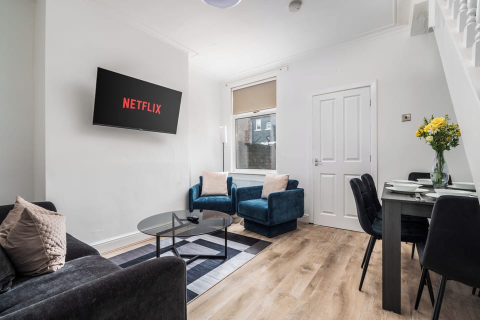 Bright and welcoming living space with a comfortable two-seater sofa and two lounge chairs. A wall-mounted Smart TV can be viewed from anywhere in the room. Dining area with a six-seater table is tucked neatly under the stairs just off the kitchen.