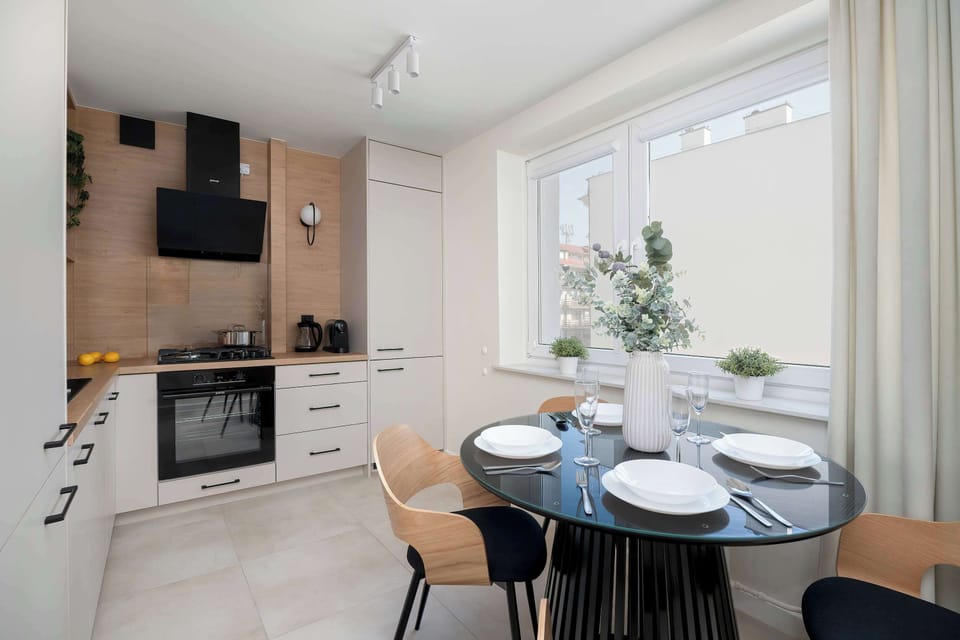A compact dining area with a round table and modern chairs. A small kitchen is visible nearby. The space is efficient and stylish.