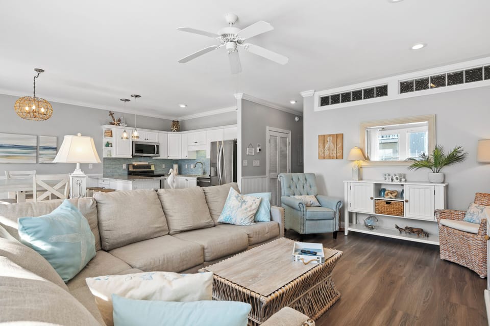 Sink into plush sofas in your bright, coastal-styled living space where gentle ceiling fans and soft lighting create the perfect atmosphere for relaxation.