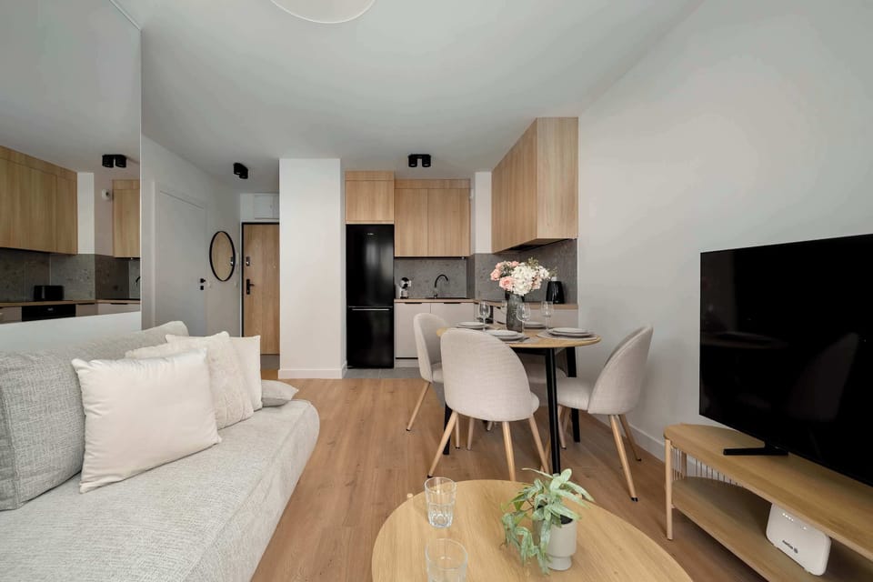 A view of the open-plan layout captures the flow from the living room toward the kitchen and hallway. The light wood flooring and white walls enhance the overall sense of space.