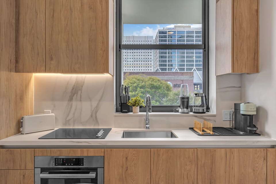 Modern efficiency meets designer style!  This sleek kitchen features warm wood cabinetry, a seamless marble backsplash, and high-end integrated appliances. With a view of the city right from the sink, it's the perfect spot to brew your morning coffee
