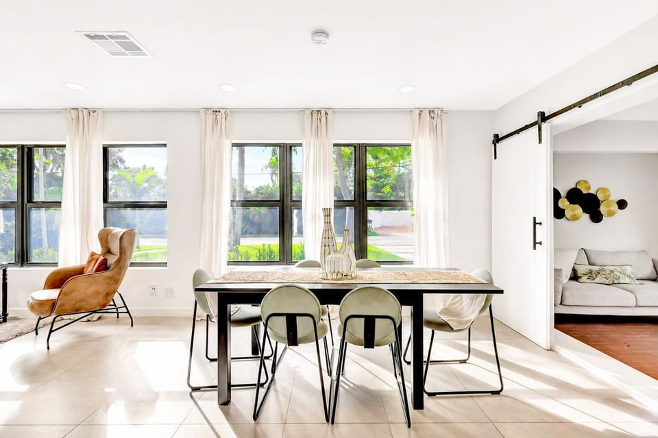 Bright, airy dining space filled with natural light, featuring a sleek modern table and soft neutral tones. Large windows create an open, relaxing feel, perfect for shared meals and quiet moments indoors.