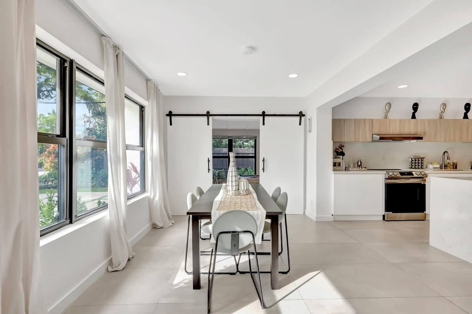 A stylish dining space with large windows and soft natural lighting. Ideal for enjoying meals together, it offers a serene indoor setting with views of the outdoors.