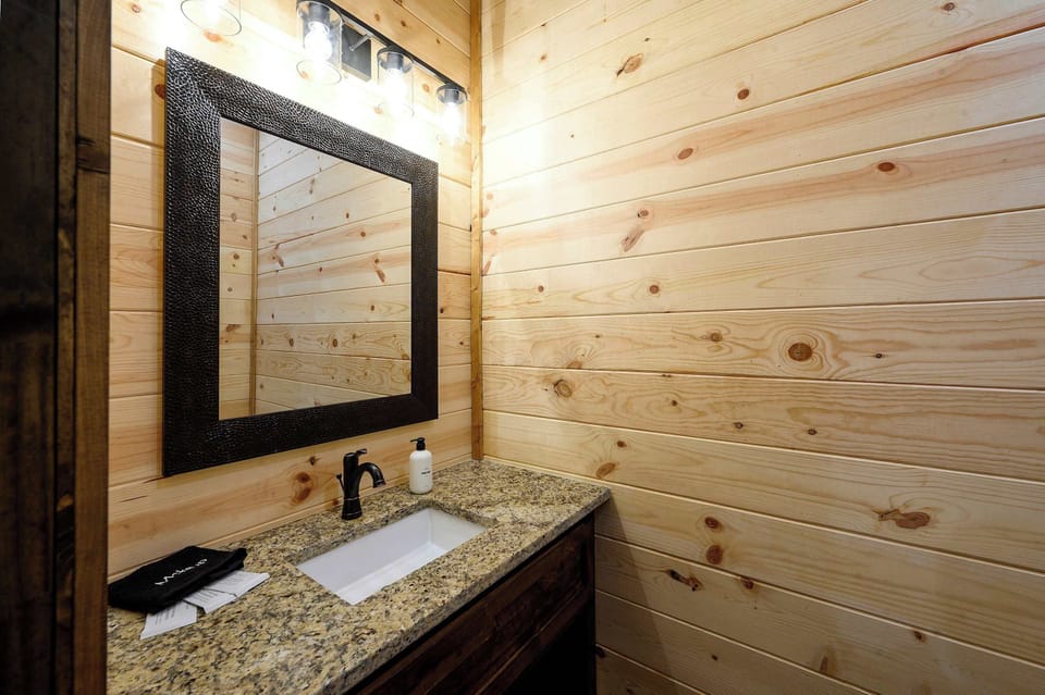 A rustic wood vanity with granite top and hammered mirror keeps this pine-lined powder bath warm and tidy. - Powder Bathroom - The Hickorybear - Broken Bow, OK