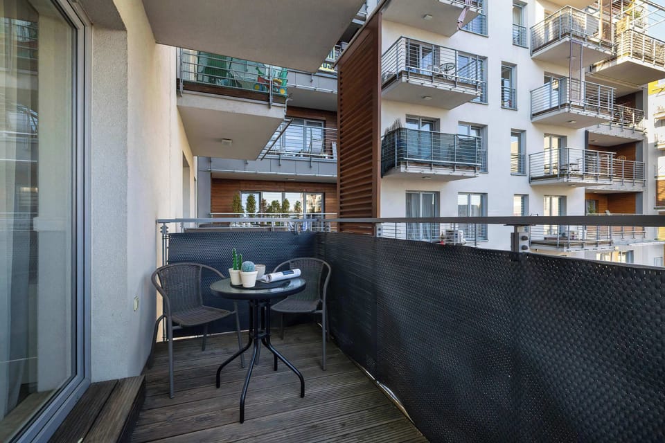 A private balcony is equipped with a small black table and chair set on wooden decking. A dark privacy screen surrounds the area, offering a quiet spot to enjoy the view.