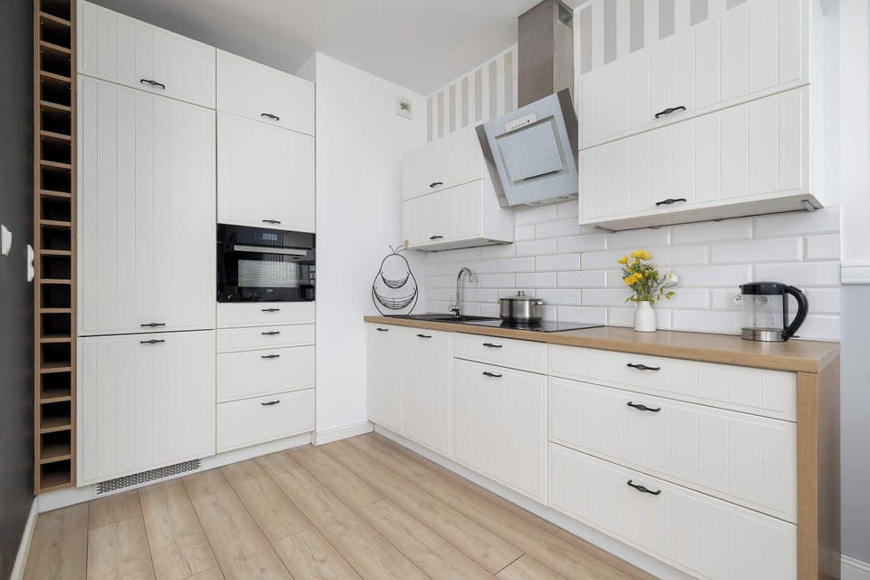 A modern kitchen with sleek white cabinets and wooden countertops, equipped with all essential appliances.  The adjacent dining table with grey chairs makes for convenient meal times.