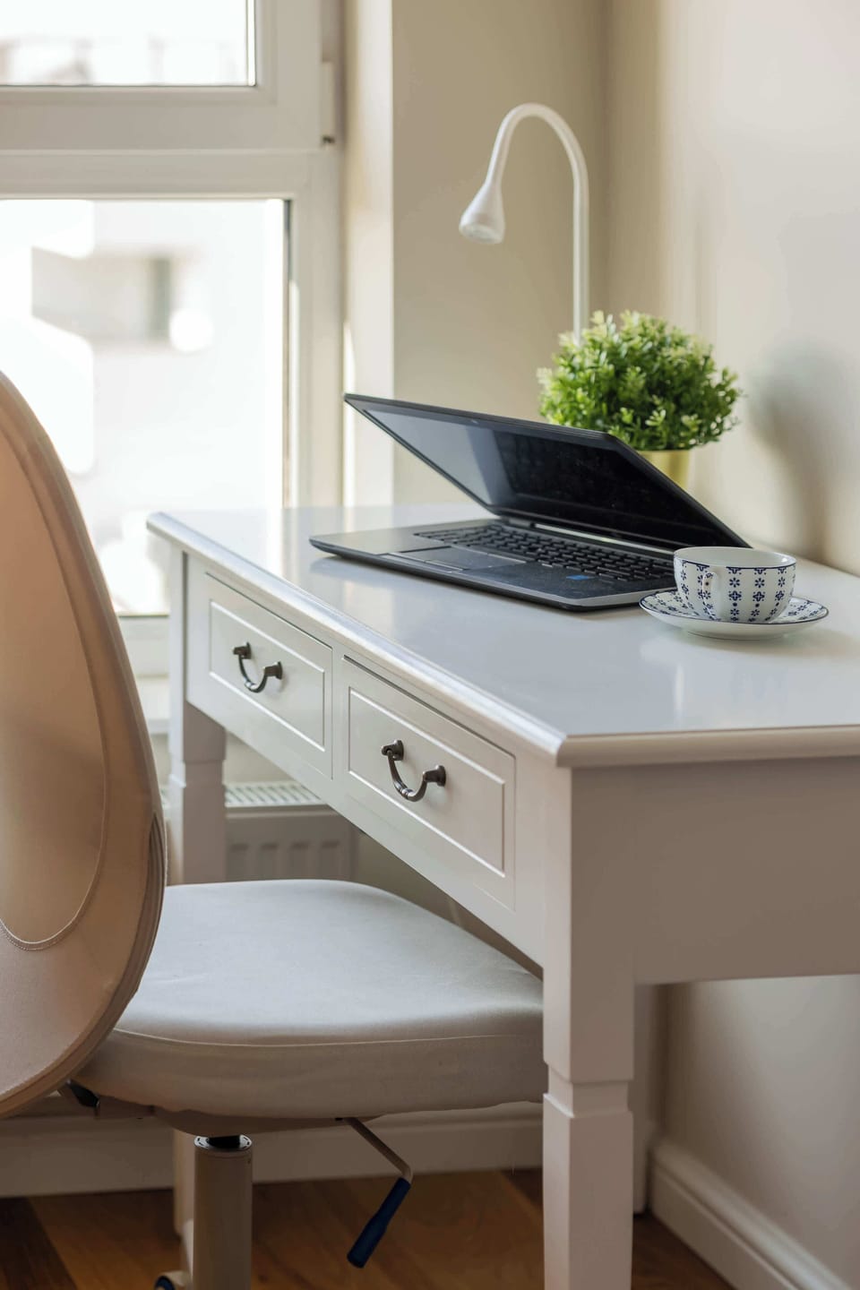 A workspace nook with a desk, chair, and a kettle on a small counter by the window.