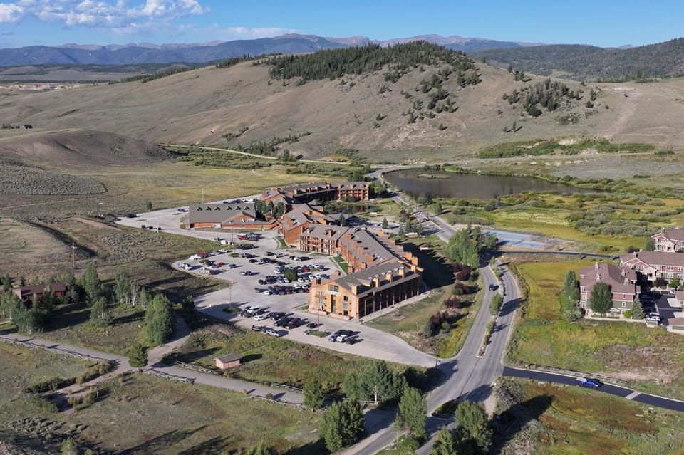 Aerial view of a mountain resort property nestled in a scenic valley with dramatic peaks and natural landscape surrounding the buildings.