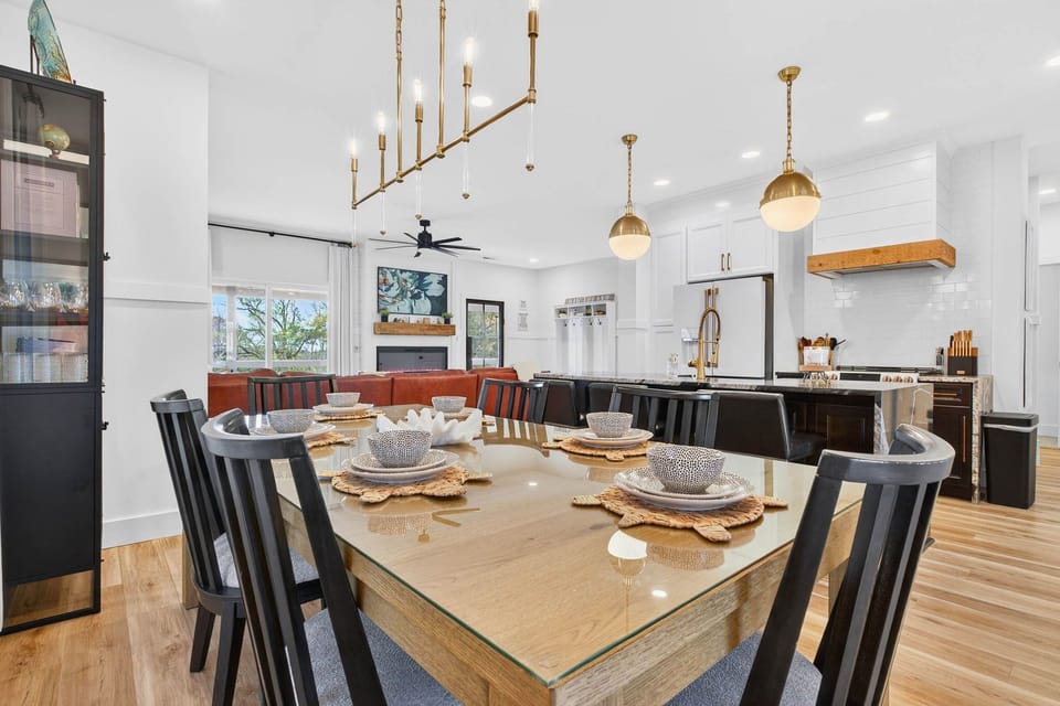 Gather around the spacious dining table set for memorable meals, highlighted by a stunning modern linear chandelier and open-concept views into the kitchen and living area.