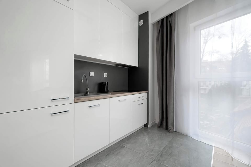 A sleek white kitchenette runs along one wall, featuring handleless cabinets and a large window that lets in light.