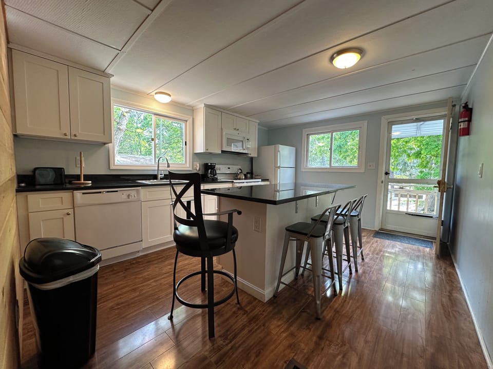 Your fully equipped kitchen features sleek granite counters, breakfast bar seating, and abundant natural light streaming through three windows overlooking the peaceful wooded surroundings.