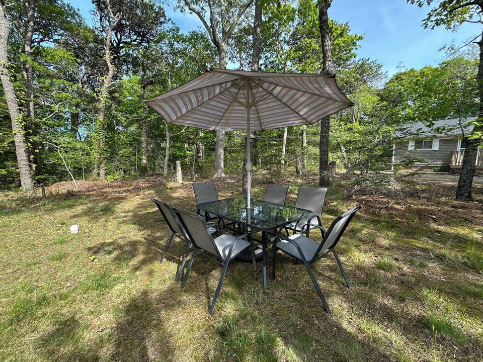 Your private outdoor dining spot awaits under the striped umbrella, surrounded by peaceful forest views for memorable meals.