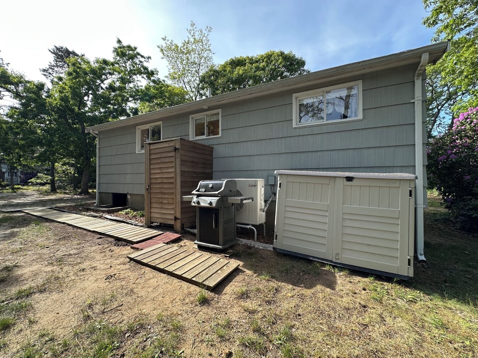 Back yard featuring BBQ grill and outdoor shower, surrounded by mature trees in a peaceful residential setting.