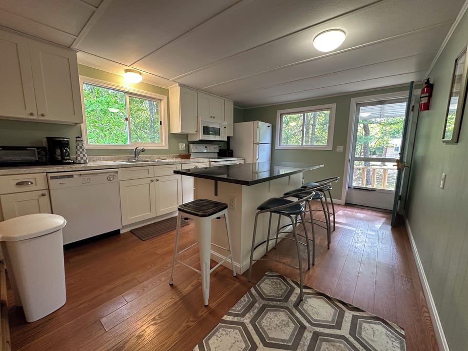 Cook your favorite meals in this bright, fully-equipped kitchen featuring white cabinetry, granite countertops, and a convenient island with modern stools.