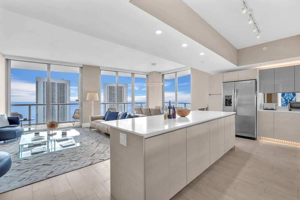 Spacious living area featuring a large flat-screen TV and a modern kitchen with a breakfast counter and stylish bar seating.