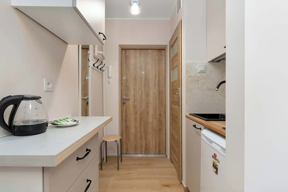 A kitchenette with white cabinets and a kettle on the counter. The space is compact.