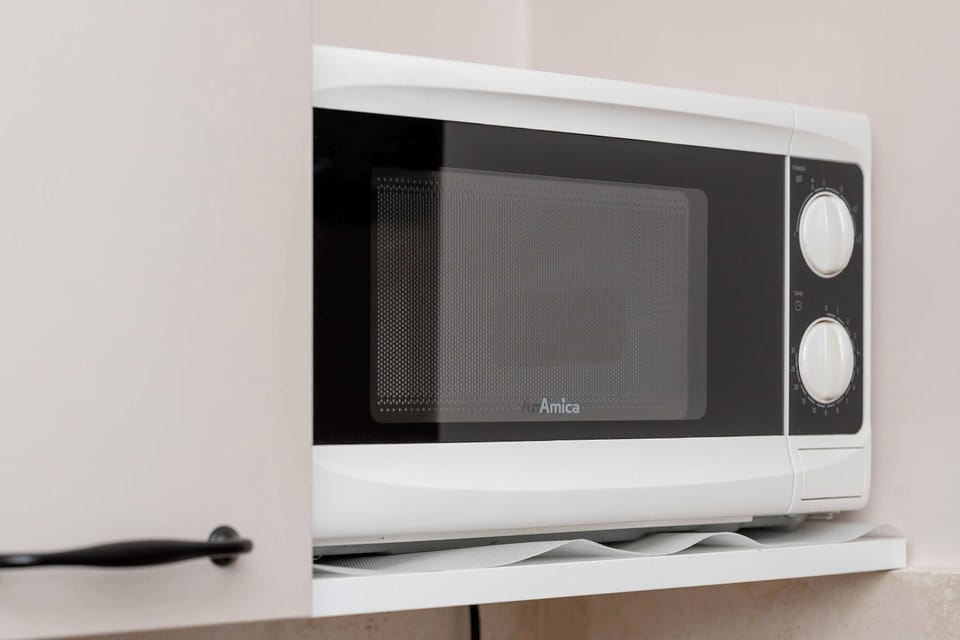 A close-up of a microwave placed on a shelf. The appliance is clean and modern with simple controls. The surrounding area is tidy and organized.