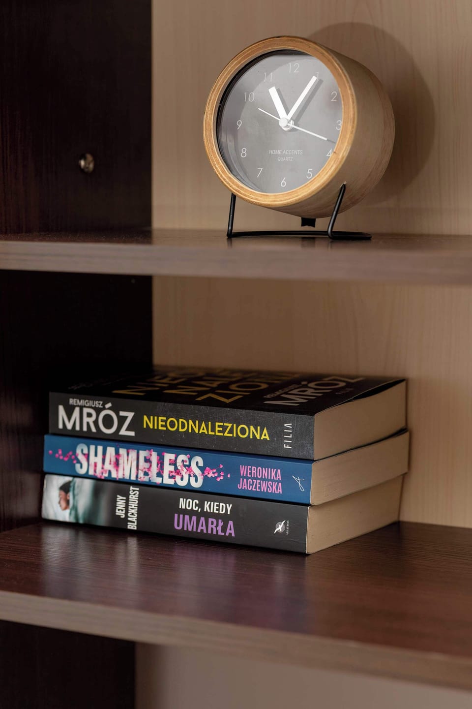 A shelf with books and a decorative clock placed on it. The items are neatly arranged for both function and decoration. The shelf is part of a larger storage unit.