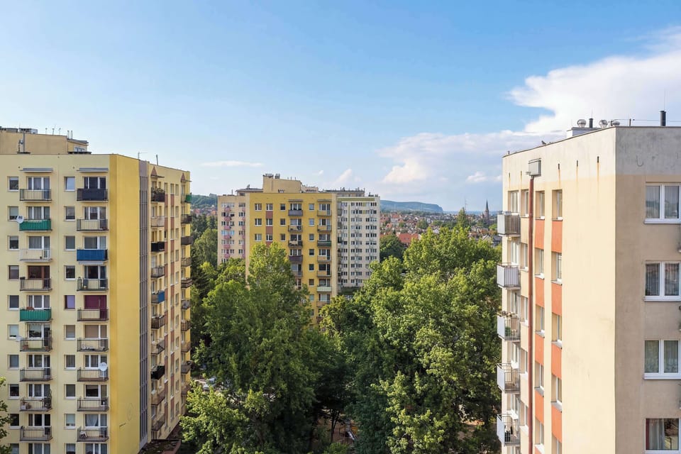 Outdoor view of residential buildings with trees and greenery below. The perspective shows multiple blocks arranged closely together. The sky is clear and bright.