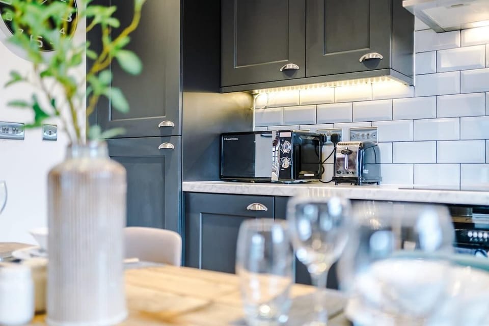 Contemporary kitchen with dark units, built-in appliances, under-cabinet lighting, and a chic dining setup.