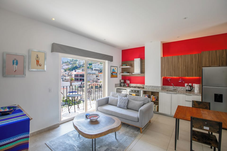 Your modern apartment features a vibrant red kitchen, cozy living area, and balcony with stunning city views for memorable evenings.