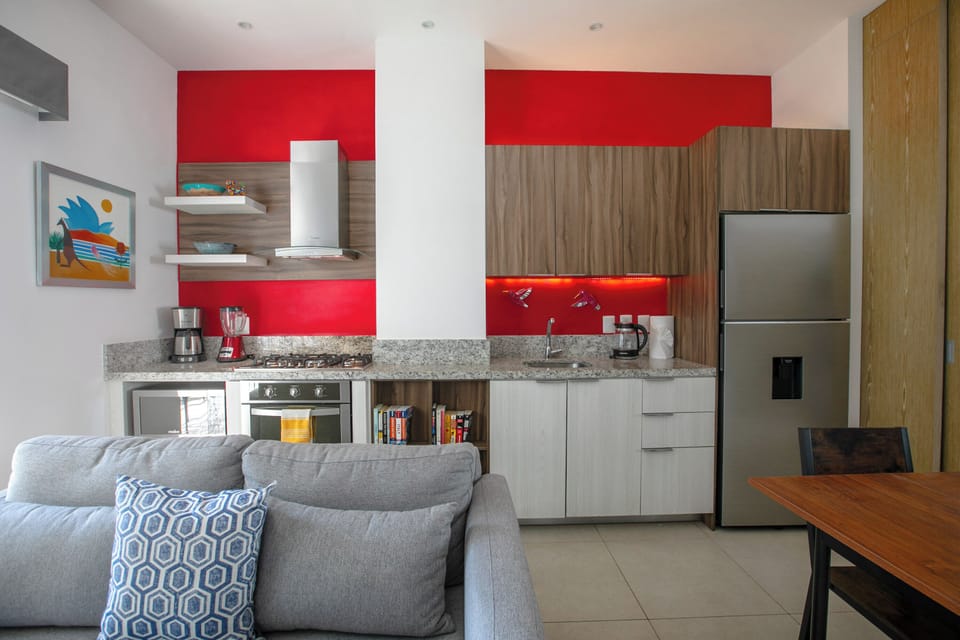 Relax on your cozy sofa while enjoying the vibrant red accent wall and fully-equipped kitchen with modern appliances.