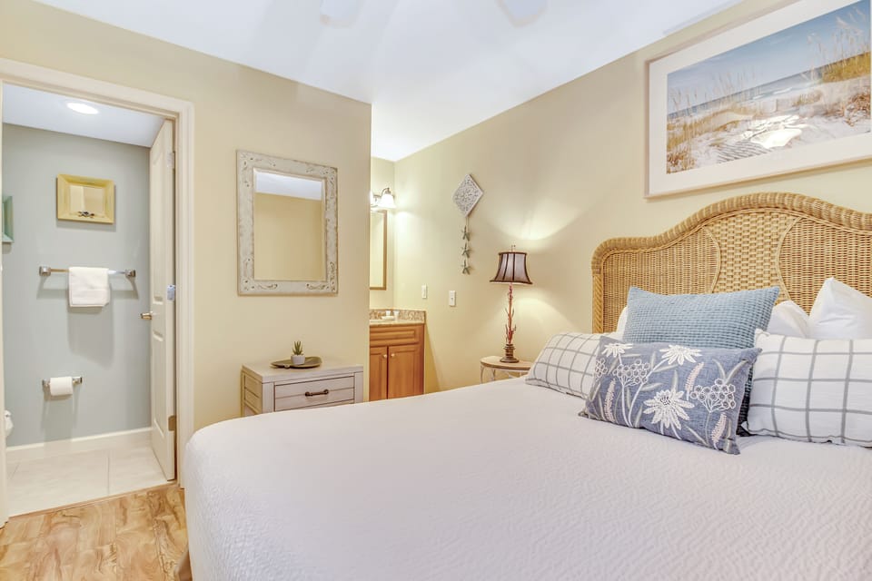 Unwind in your charming bedroom featuring a wicker headboard, soft coastal linens, and convenient ensuite access for ultimate comfort.