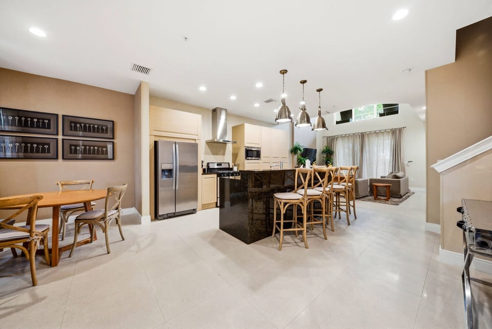 This bright, airy kitchen boasts sleek cabinetry and a spacious dark granite island, perfect for gathering. The light walls enhance the natural light, creating an inviting atmosphere for meals and conversation.