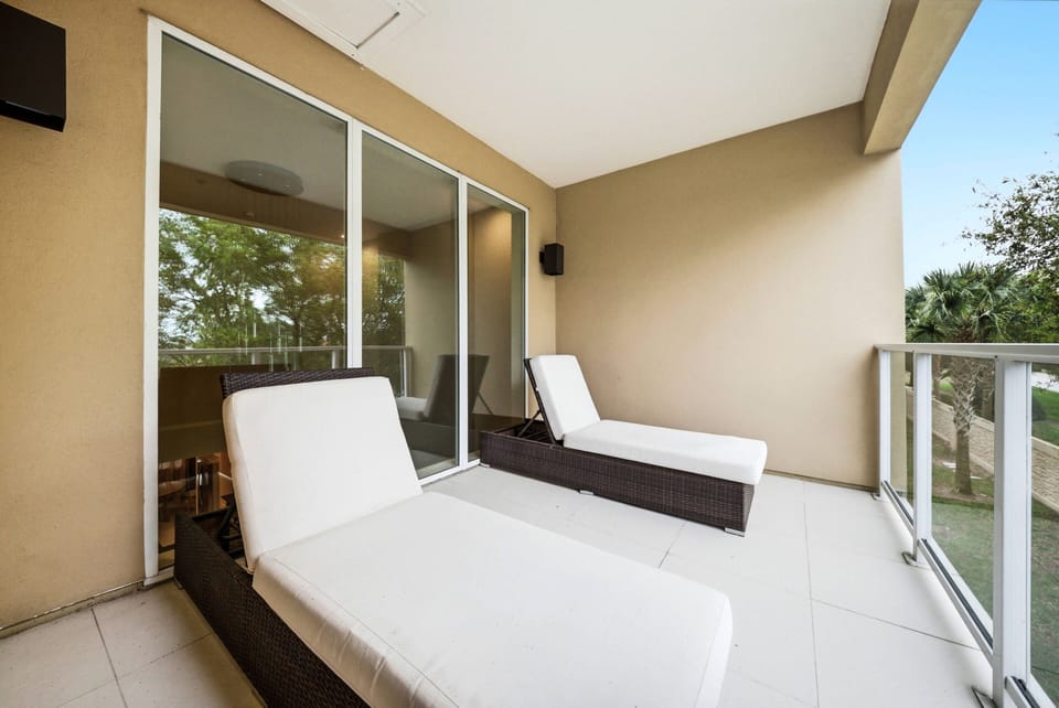 Step onto your private balcony, where modern white loungers beckon you to bask in the sunlight. The glass railing provides a clear view of the lush greenery, creating a serene outdoor oasis for your relaxation.