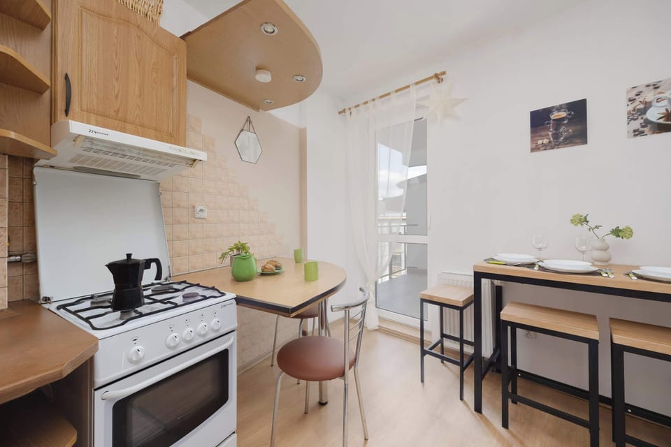The kitchen's workspace is shown with a stove, tiled backsplash, and wooden cupboards stocked with kitchenware.
