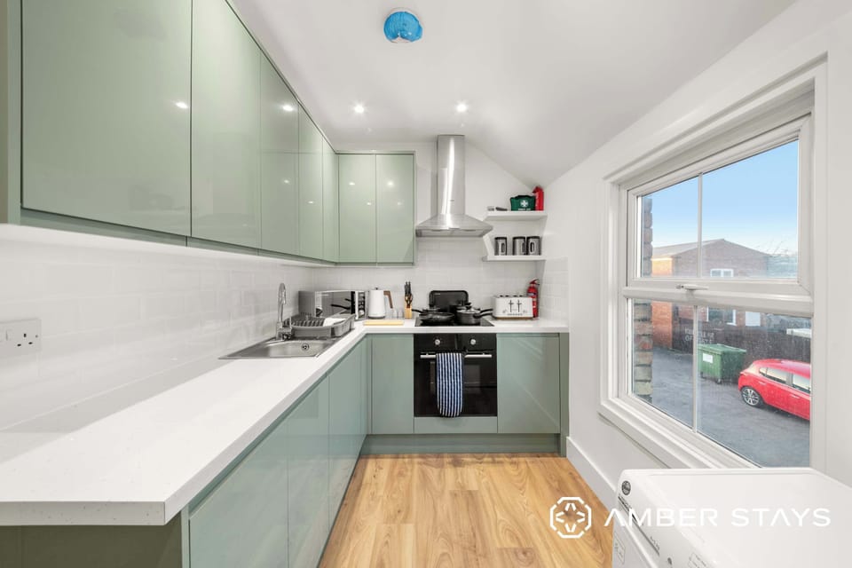 A kitchen features light green cabinets, a white countertop with a built-in stove and sink, and a large window looking outside.
