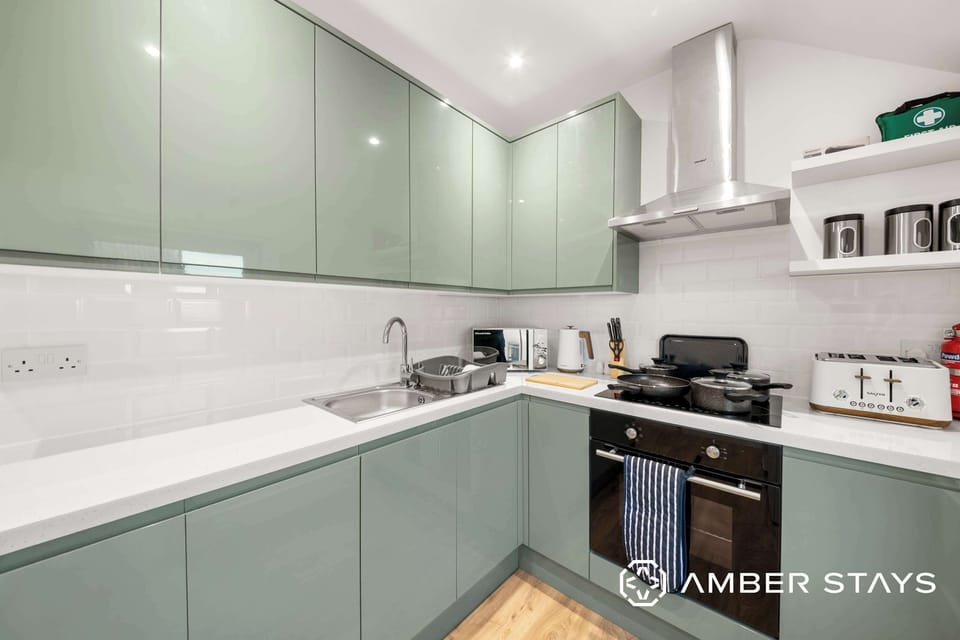A kitchen features light green cabinets, a stainless steel sink, and an integrated oven under a silver range hood.