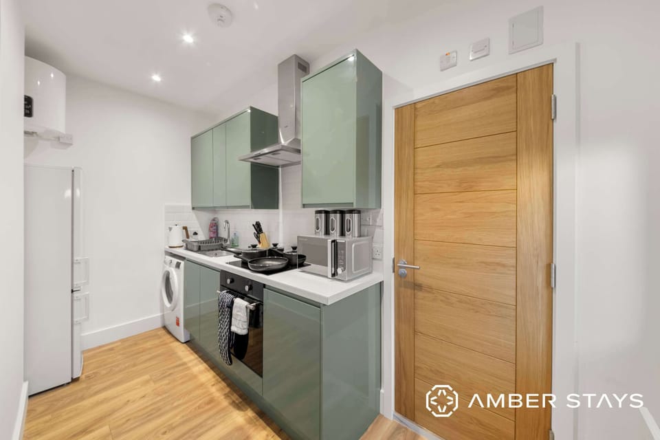 A kitchen features green cabinets, a light wood door on the right, integrated appliances, and a washing machine next to the counter.