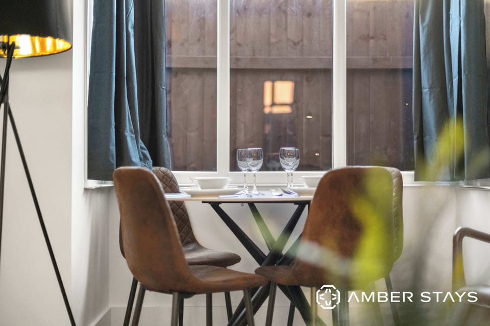 A dining area features brown leather chairs around a small table set with wine glasses in front of a large window.