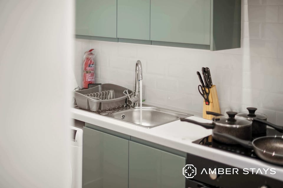 A kitchen features grey cabinets, a stainless steel sink with a drying rack, and pots sitting on a black stovetop.