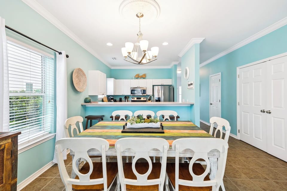 Gather around this bright dining space where coastal charm meets comfort. Soft turquoise walls and elegant chandelier create the perfect setting for your memorable meals together.