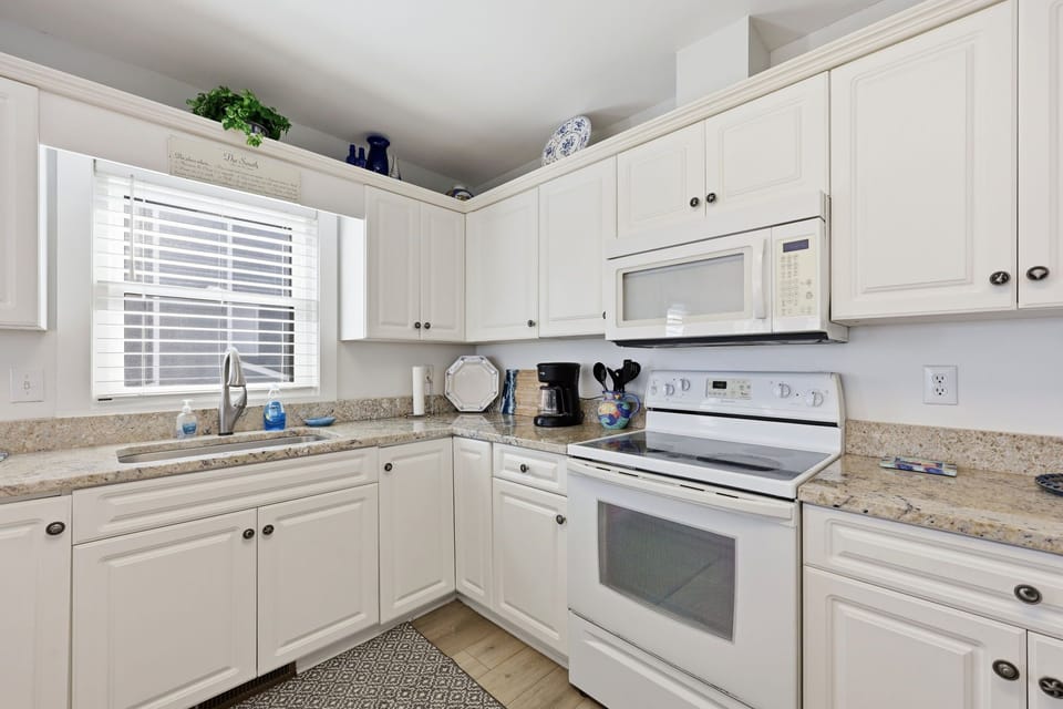 Your fully equipped kitchen invites easy meal prep with granite countertops, white cabinetry, and modern appliances bathed in natural light from the window.
