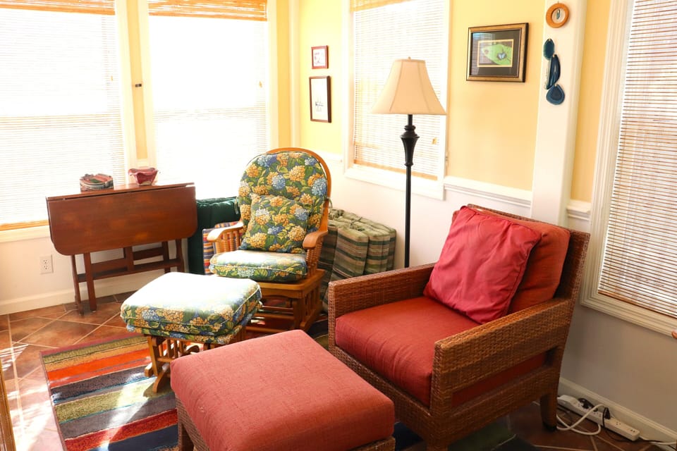 Sink into comfortable wicker seating with colorful cushions, where natural light floods through bamboo blinds in your cozy living space.