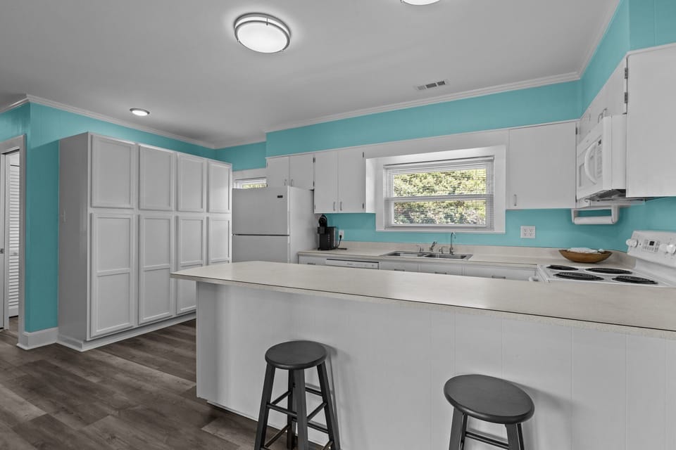 Your bright kitchen features modern white cabinets, cheerful turquoise walls, and a breakfast bar where you can enjoy morning coffee together.
