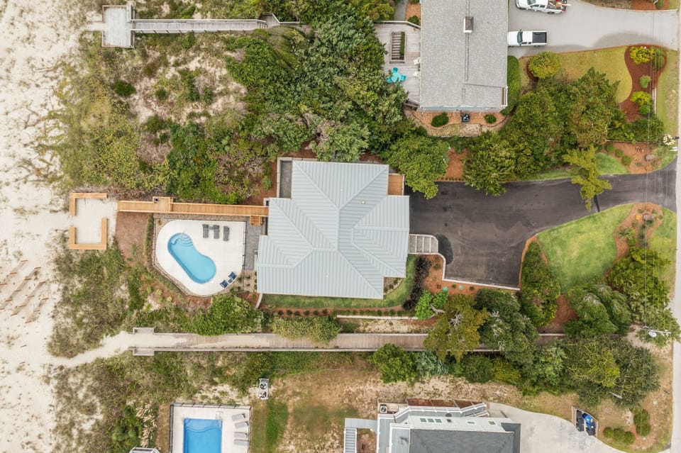 Aerial view of vacation rental property with private pool and landscaped grounds surrounded by mature trees and neighboring homes.