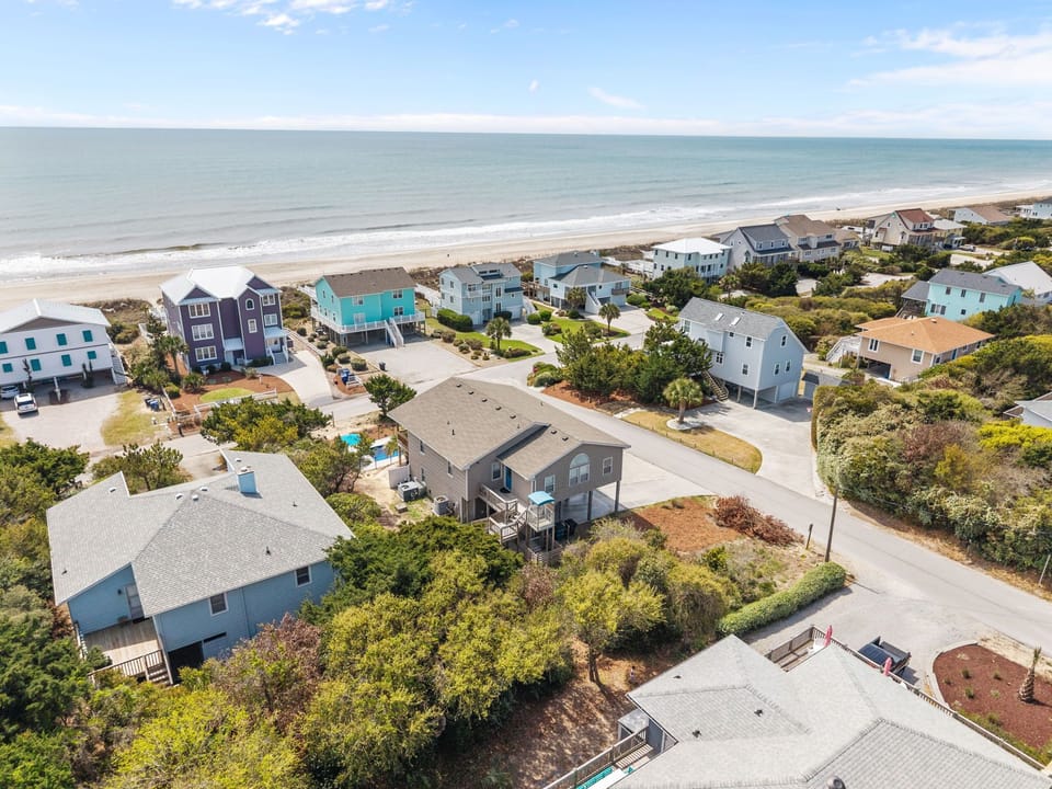 Aerial view of beachfront vacation homes nestled among coastal vegetation, just steps from pristine sandy shores and rolling ocean waves.