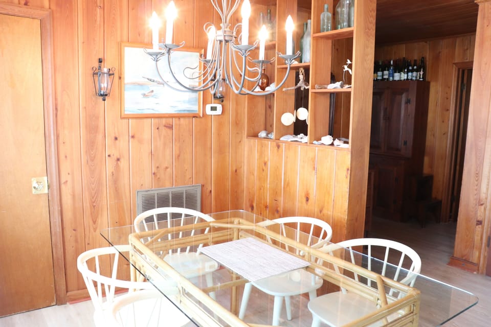 Gather around your elegant glass dining table beneath the warm chandelier glow, surrounded by rich wood paneling that creates an intimate atmosphere.