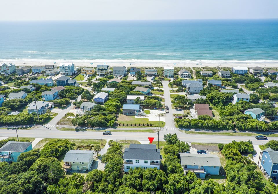 Aerial view of a beachfront vacation rental community with white sand beach and coastal homes surrounded by lush greenery.