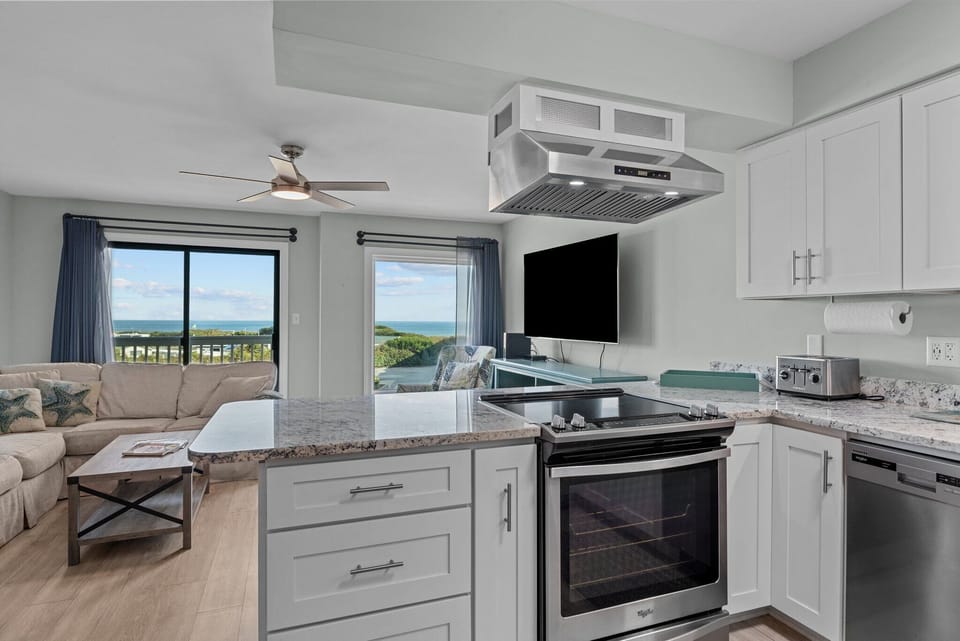 Your open kitchen flows seamlessly into the living space, where ocean views through large windows create the perfect backdrop for cooking and relaxing.