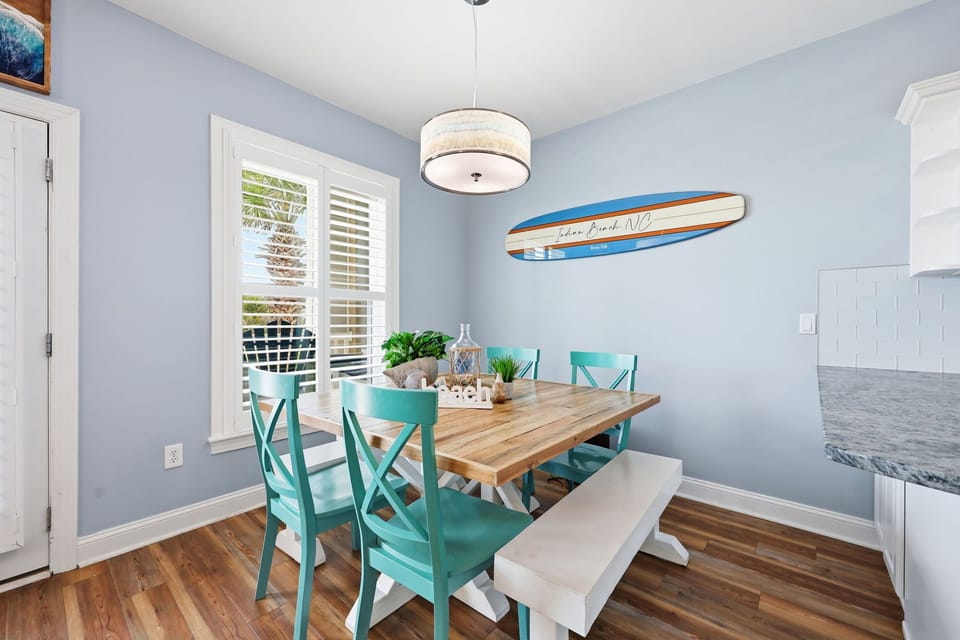 Picture yourself sharing meals at this charming coastal table, where turquoise chairs and beachy surfboard décor create a laid-back vibe. Sunshine streams through plantation shutters as you enjoy your morning coffee.