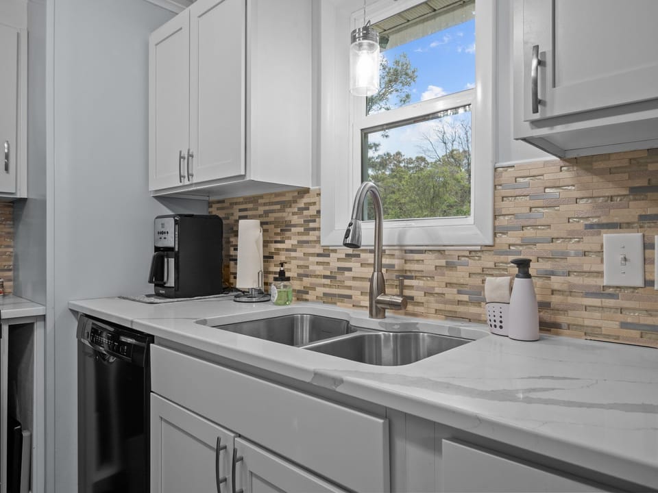 Your modern kitchen features gleaming countertops, stainless steel appliances, and a mosaic tile backsplash, with natural light streaming through the window.
