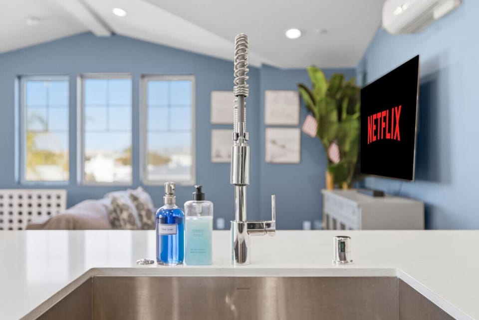 Quartz kitchen island with deep stainless steel sink and commercial-style pull-down faucet — open views to the living room and Smart TV from the kitchen