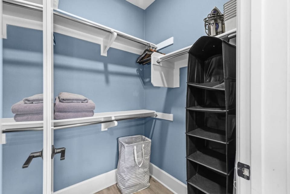 Primary bedroom walk-in closet with double hanging rods, built-in shelving, shoe organizer, laundry hamper, and iron — ample storage for an extended stay
