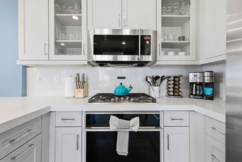 Kitchen cooking station with 5-burner gas range, stainless steel microwave, full knife set, spice rack, and Cuisinart coffee maker — everything you need to cook in