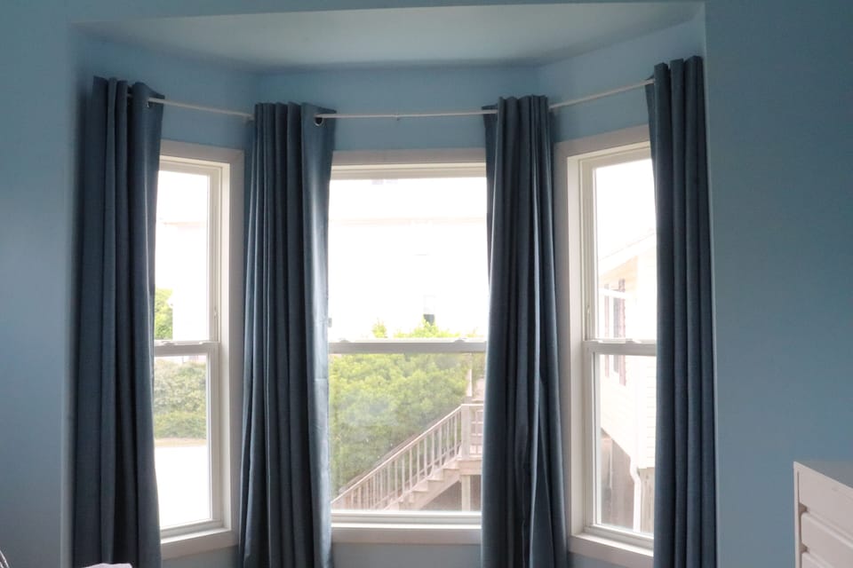 Bright bay windows frame a peaceful neighborhood view, with soft curtains offering privacy. Your retreat to relax and watch the world outside unfold.